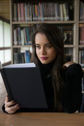Woman sitting along bookshelves and holding open book