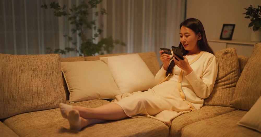 Young South Korean Woman Using Online Shopping App in a Cozy Apartment, Making Secure Purchases with Her Smartphone
