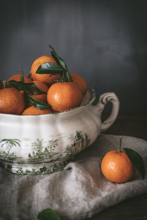 Orange tangerines in ceramic ornamental bowl on wooden table