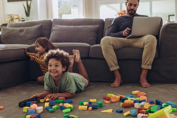 Man working on laptop sitting at home with kids playing on the floor