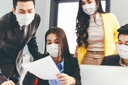 Office full of colleagues in facemasks discussing work