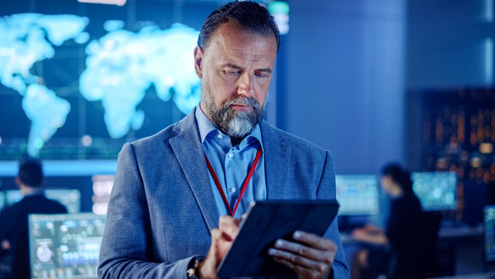 Focused Man in a High-tech Control Room Analyzes Data on a Tablet
