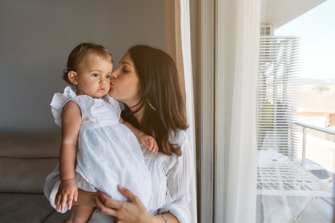 Woman kissing daughter on cheek while standing near window