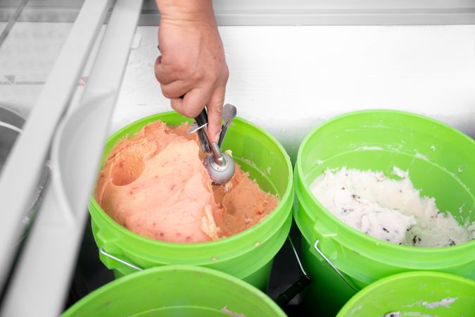 An Hispanic adult woman is taking mamey ice cream with a spoon from a bucket. Close up