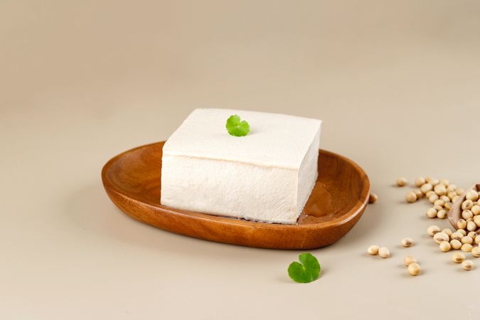 Tofu block on wooden plate with garnish and soybeans