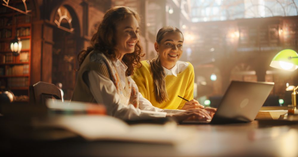 Joyful White and Hispanic Female Students Collaborating on a Project in a Vintage Library.