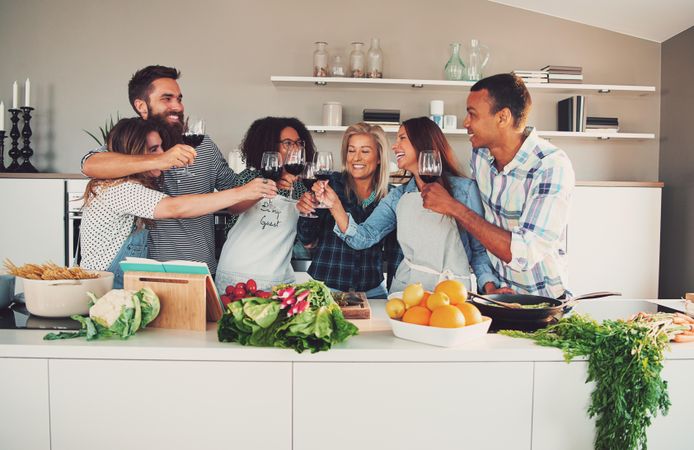 Happy diverse friends toasting with red wine in the kitchen