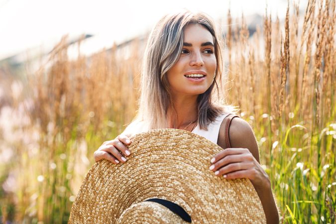Happy woman standing in field outside holding her sunhat