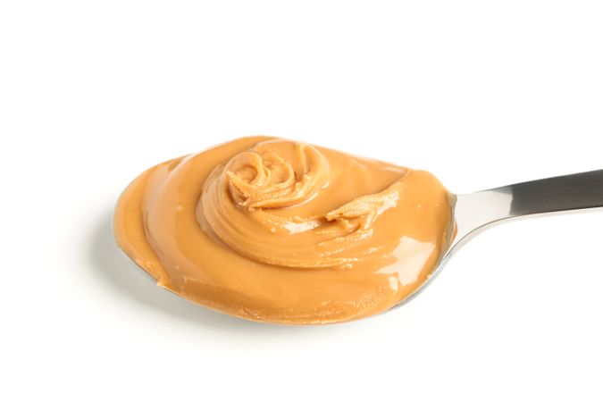 Creamy peanut butter in spoon isolated on light background, closeup. A traditional product of American cuisine