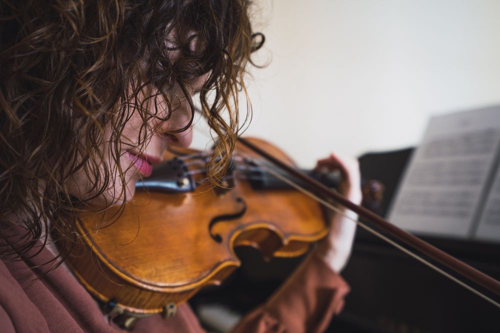 Pregnant woman playing on violin near piano in room
