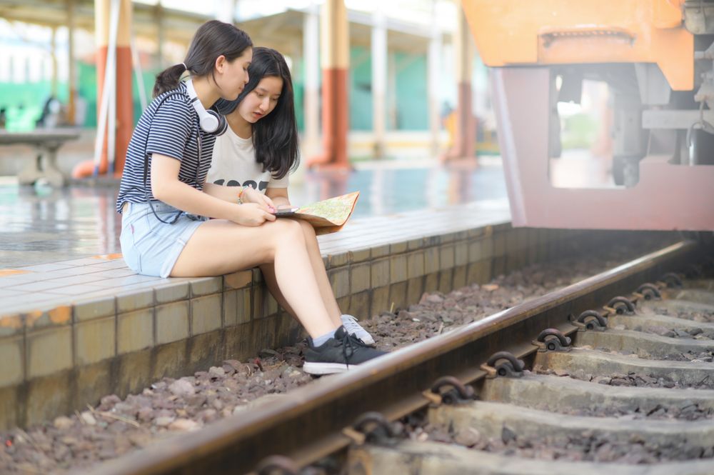 Two female travelers look at maps on a train platform