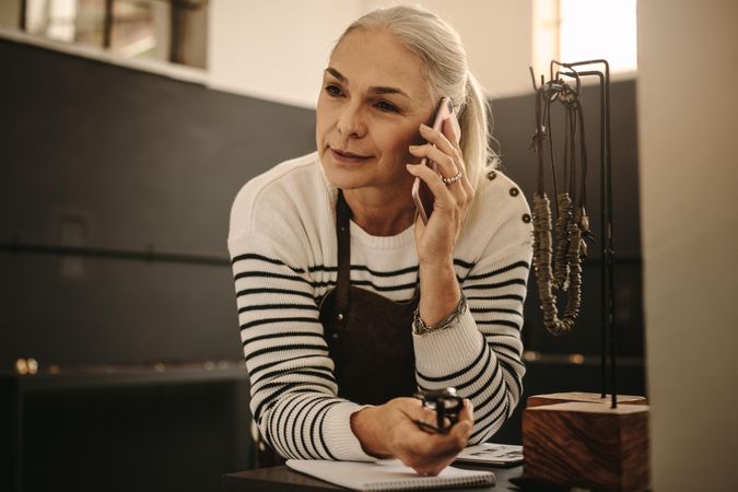 Portrait of woman jewelry maker leaning to desk and talking on cell phone