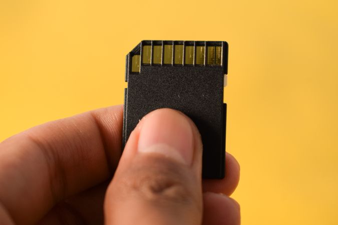 Close up of SD card in hand with yellow background and space for text