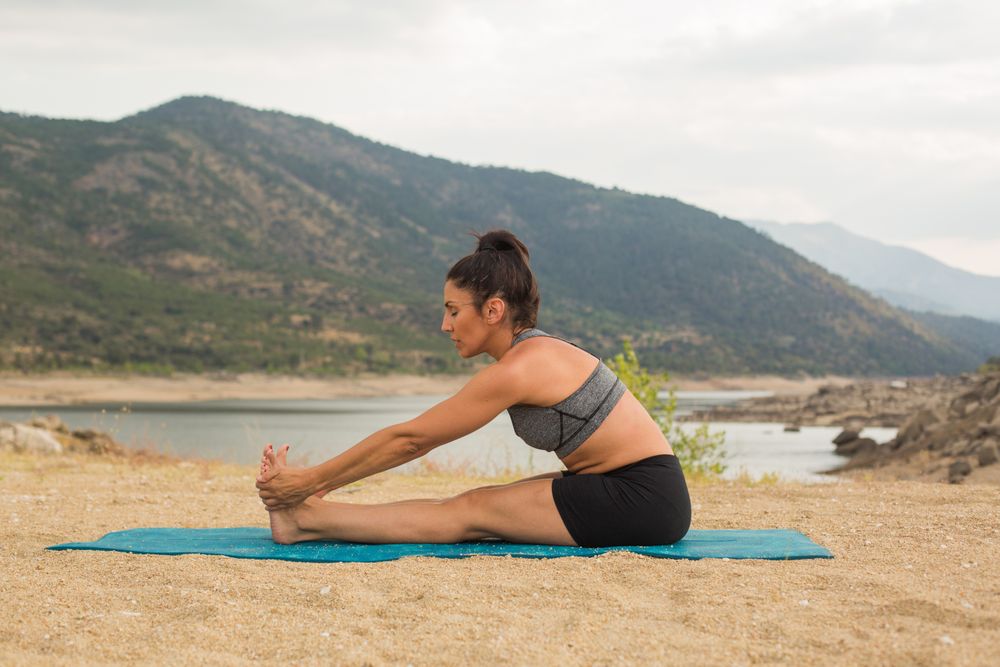 Woman practicing yoga outdoors near water