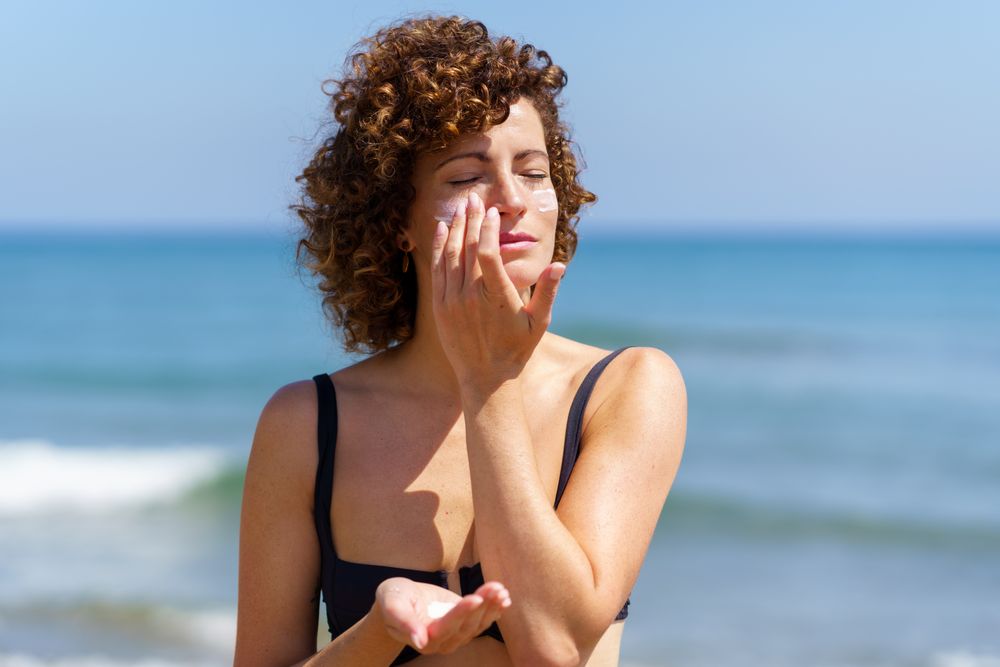 Young female smearing cream on face protecting from sunburn