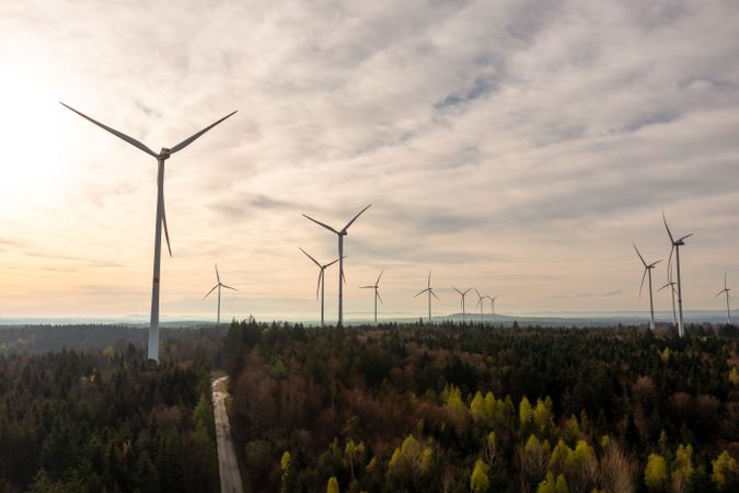 Drone aerial view with wind turbines farm inside a forest at sunrise