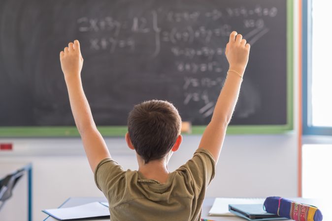 Back of teenager with arms up in celebration in class