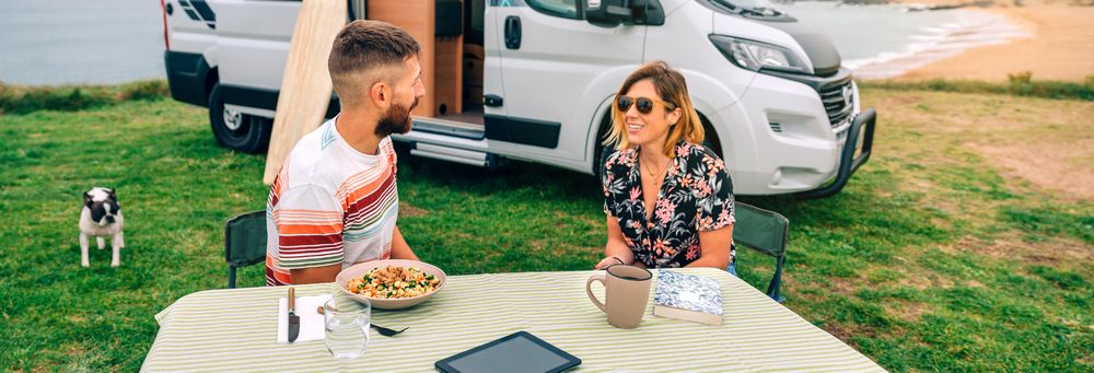 Male and female sitting at table outside parked motorhome