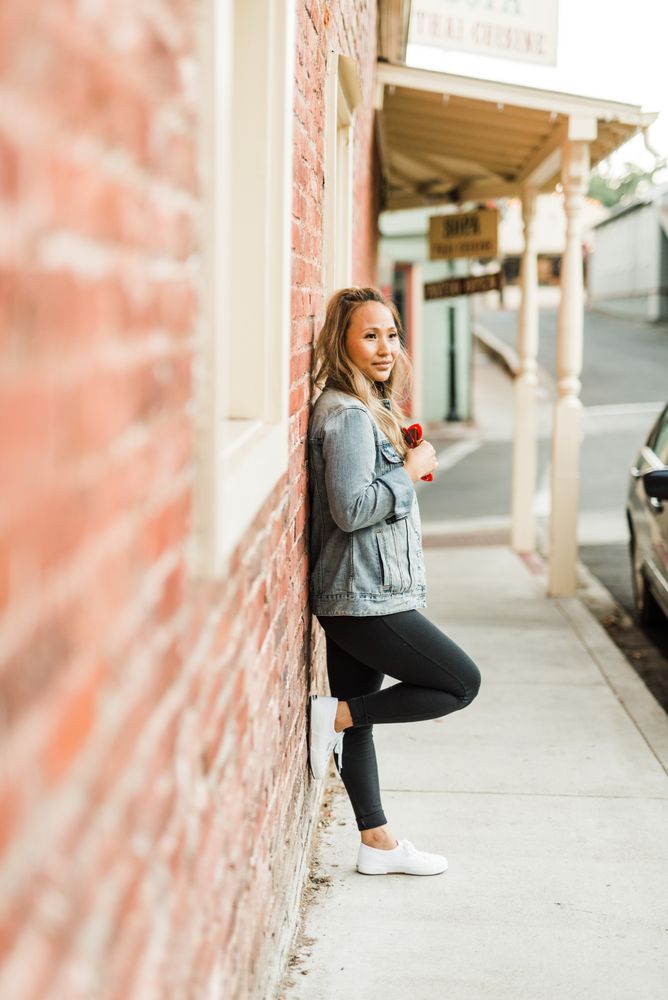 Side view of woman in denim jacket leaning on a red brick wall