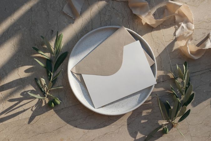 Blank greeting card, envelope mock up on ceramic plate in sunlight with olive branch