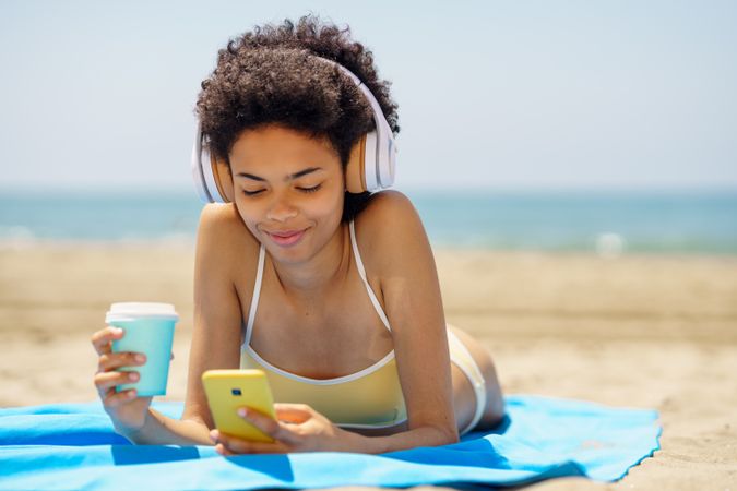Female with curly hair on beach towel using her phone