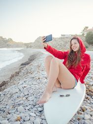 Smiling woman taking selfie lying on surfboard