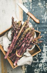 Close up of bunches of purple asparagus, knife on blue background, vertical composition