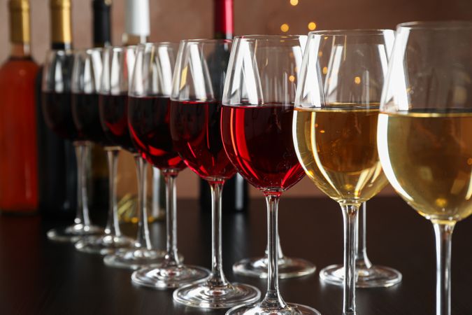 Bottles and glasses with wine on dark table, blurred lights, closeup