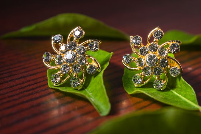 Close-up of beautiful luxury diamond earrings on green leaves with a wood background