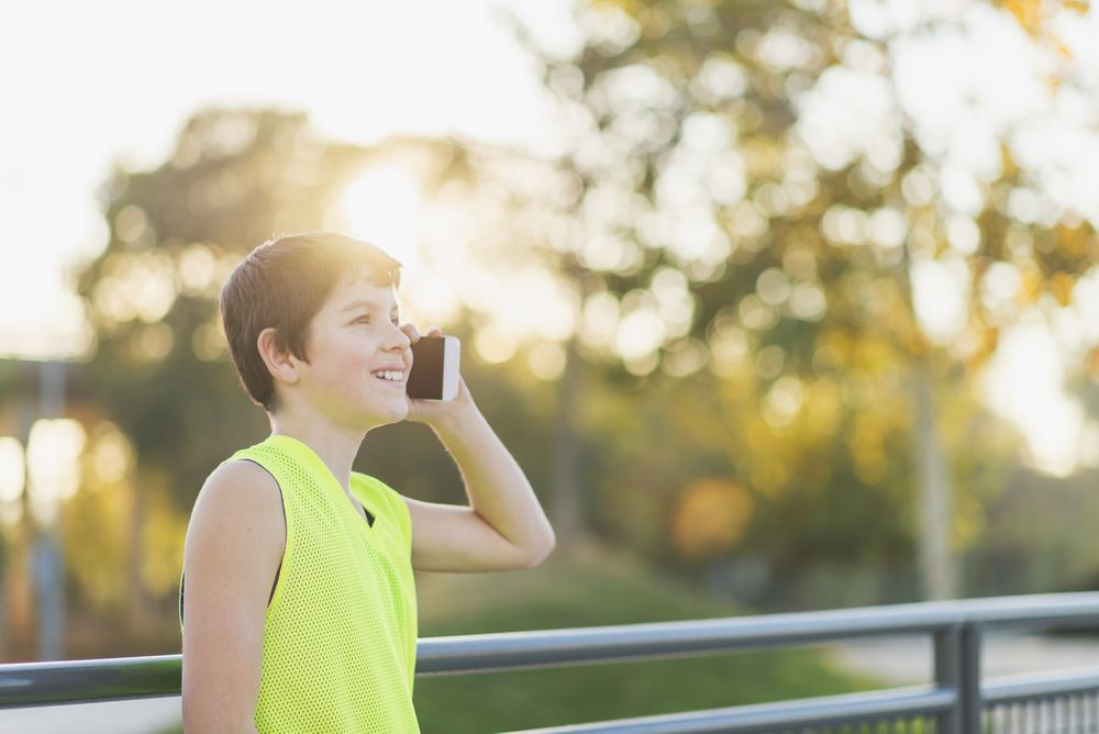 Young male teen calling by phone outdoors at sunset