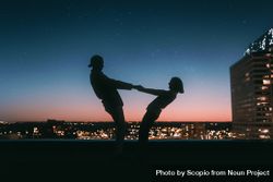 Silhouette of man and woman holding hands standing on rooftop near city at sunset 5oo385