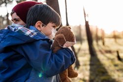 Father holding son with facemask and holding teddy bear