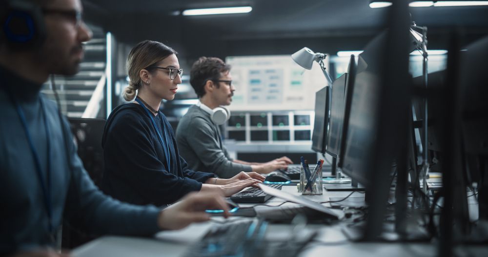 Focused Young Multiethnic Female Software Developer Working on Computer Together with Two Creative Male Colleagues.
