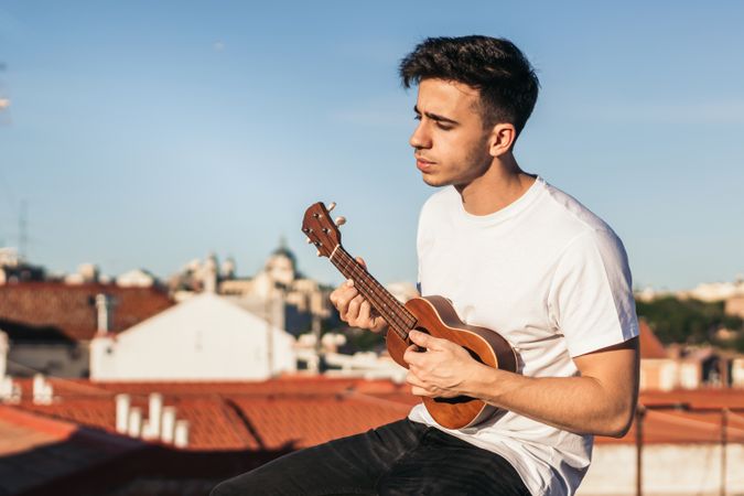young man sitting playing ukelele on a rooftop