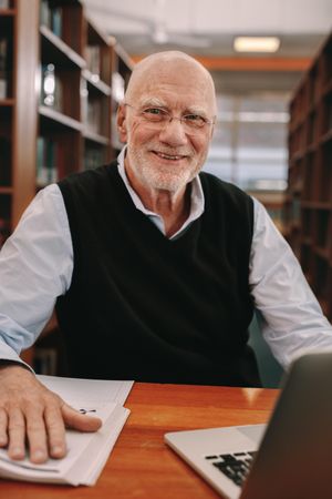 Smiling older man sitting in library with college materials