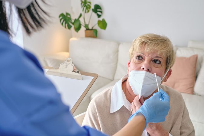 Crop physician with cotton swab against mature patient at home