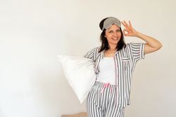 Woman making OK sign with hand, holding pillow in bed.