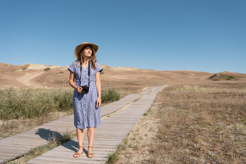 adult woman in straw hat and dress with camera standing on country path