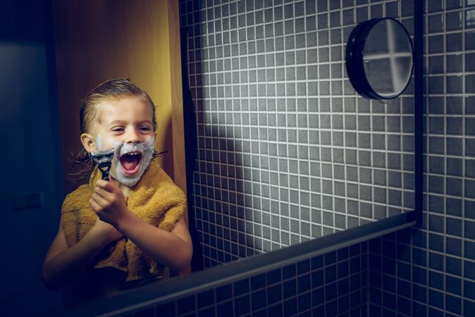 Happy boy with shaving razor in bathroom