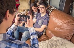 Friend taking photos to couple on a sofa