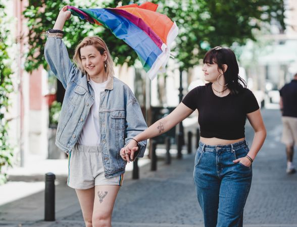 Lesbian couple with LGBT flag walking on street