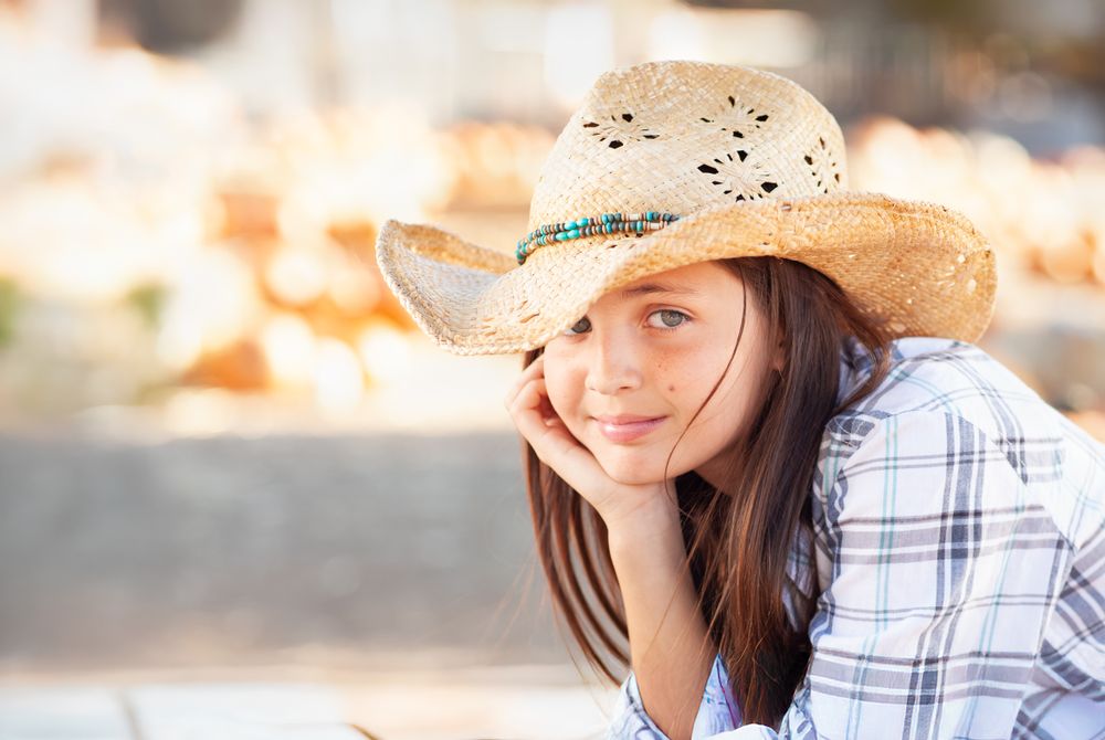 Girl Wearing Cowboy Hat Enjoying The Pumpkin Patch on a Sunny Fall Day.