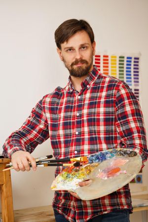 Male artist in red plaid shirt holding paint palette