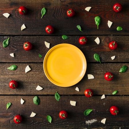 Basil, tomatoes, and cheese on wooden background with plate