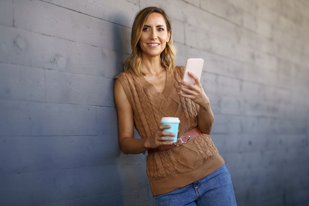 Stylish female with coffee browsing cellphone