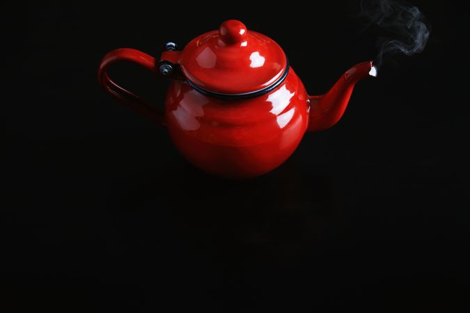 Shiny red tea pot on dark table with steam rising from spout