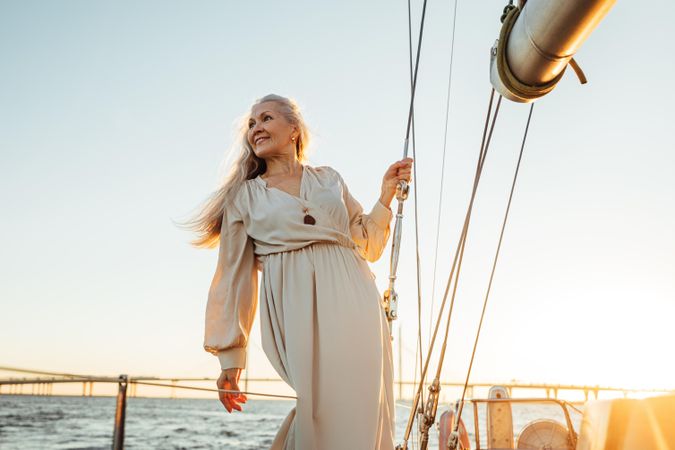 Older radiant woman in a dress on a sailboat at dusk