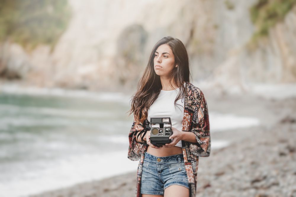 Woman with camera on shore near stones and water