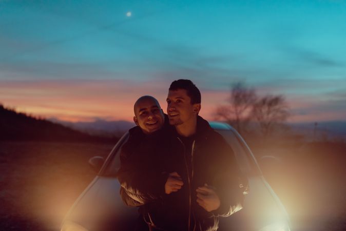 Men hugging on field near car at night
