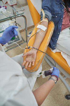 Crop nurse in scrubs performing blood donation on anonymous woma